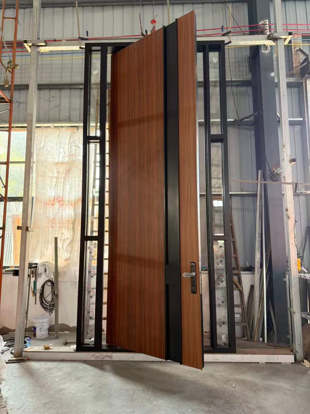 Walnut-finish pivot door swung open on its pivot inside a black steel frame with glass sidelites