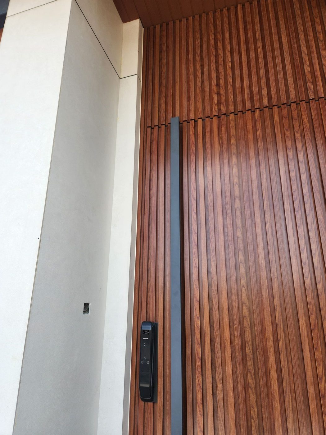 Close-up of a full-height wood-slat pivot door with a black full-length pull and smart lock