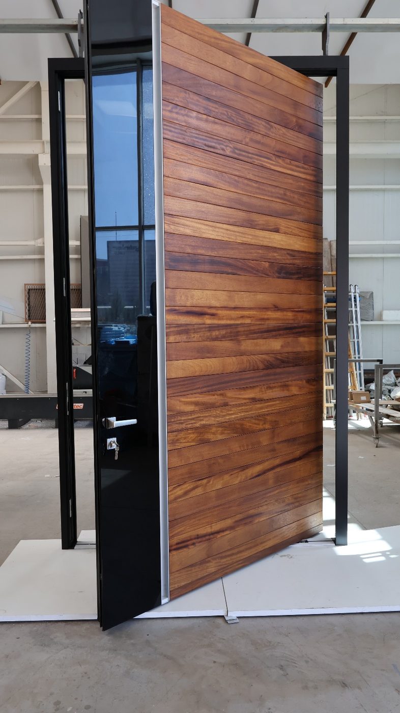 Horizontal hardwood-plank pivot door with a gloss black edge panel, shown open
