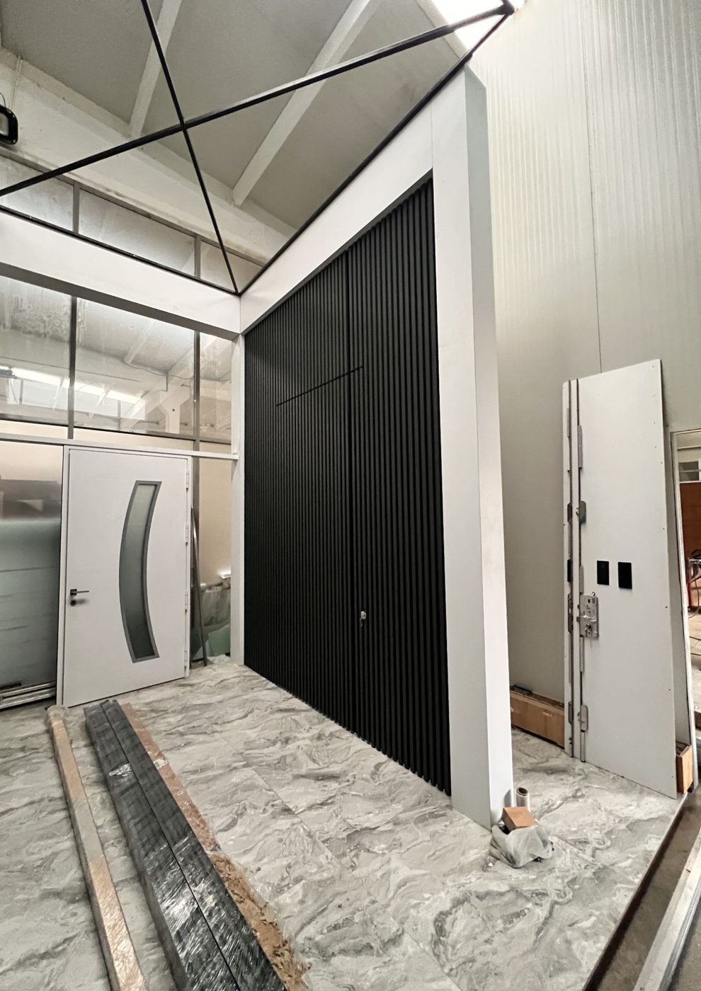 Oversized black slatted pivot door set in a tall white portal frame