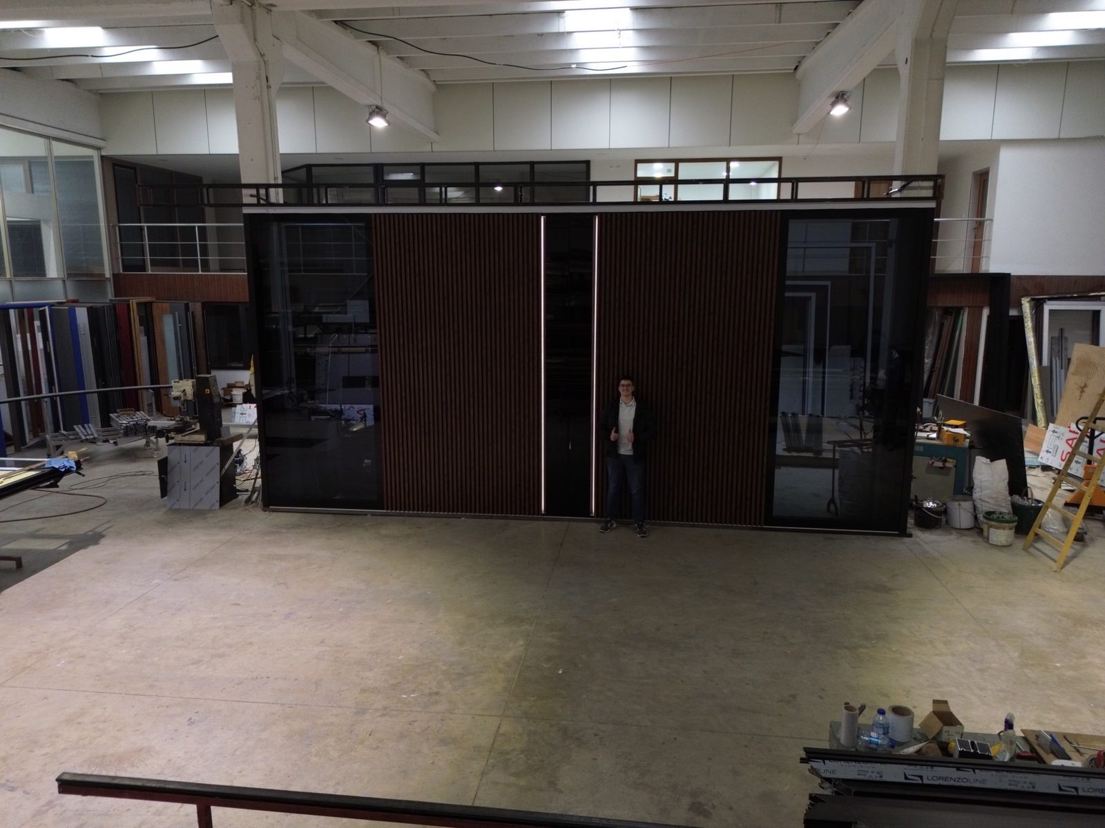 Wide entry wall of wood-look slats, black glass panels and lit vertical reveals, with a person standing in front for scale