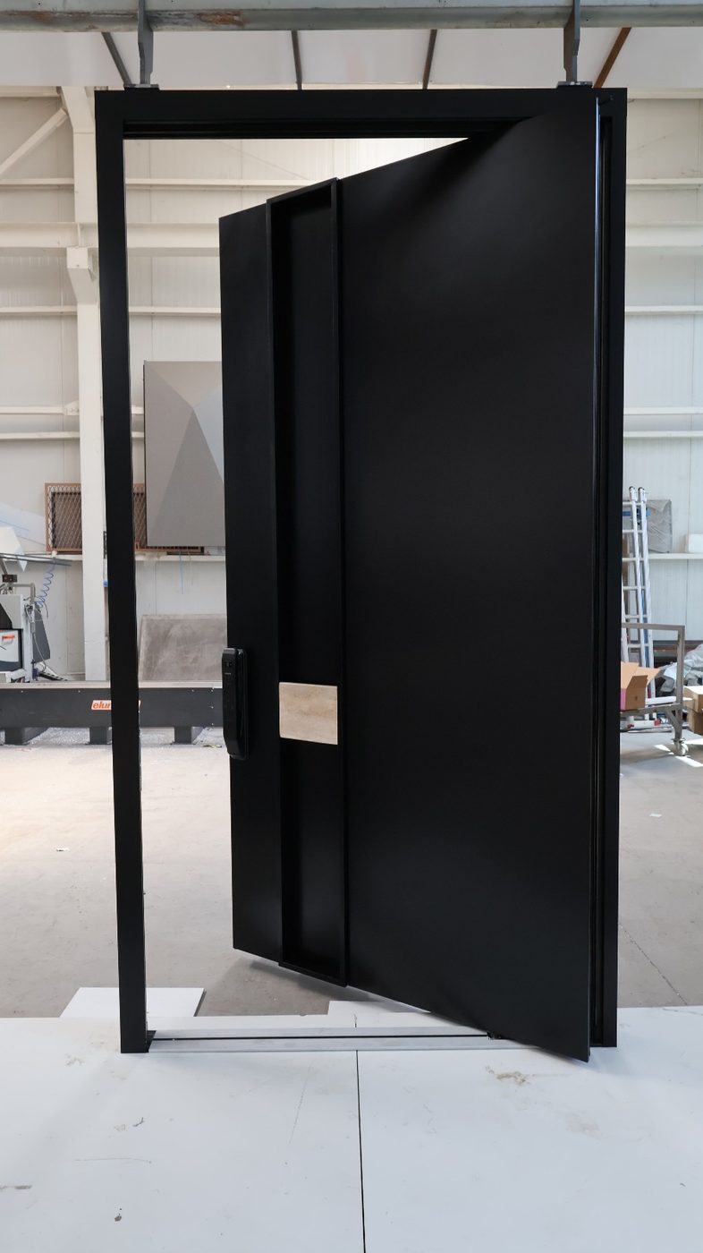 Matte black pivot door with a recessed full-height pull and stone accent, shown open in a black frame