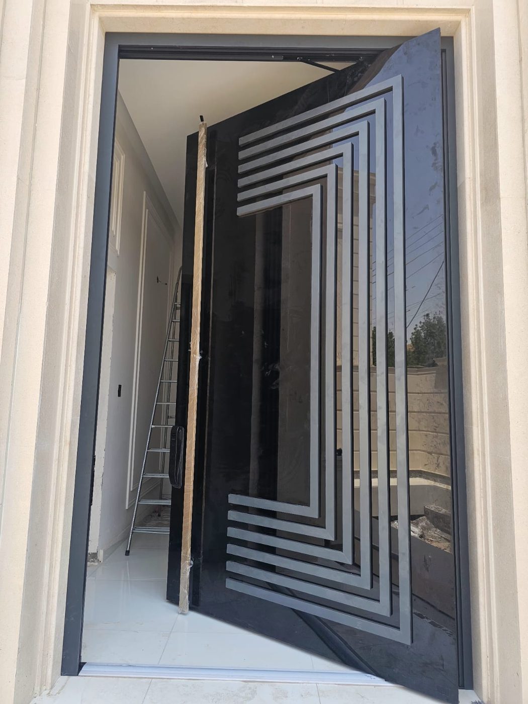 Gloss black pivot door with a raised stepped geometric pattern, open in a stone surround