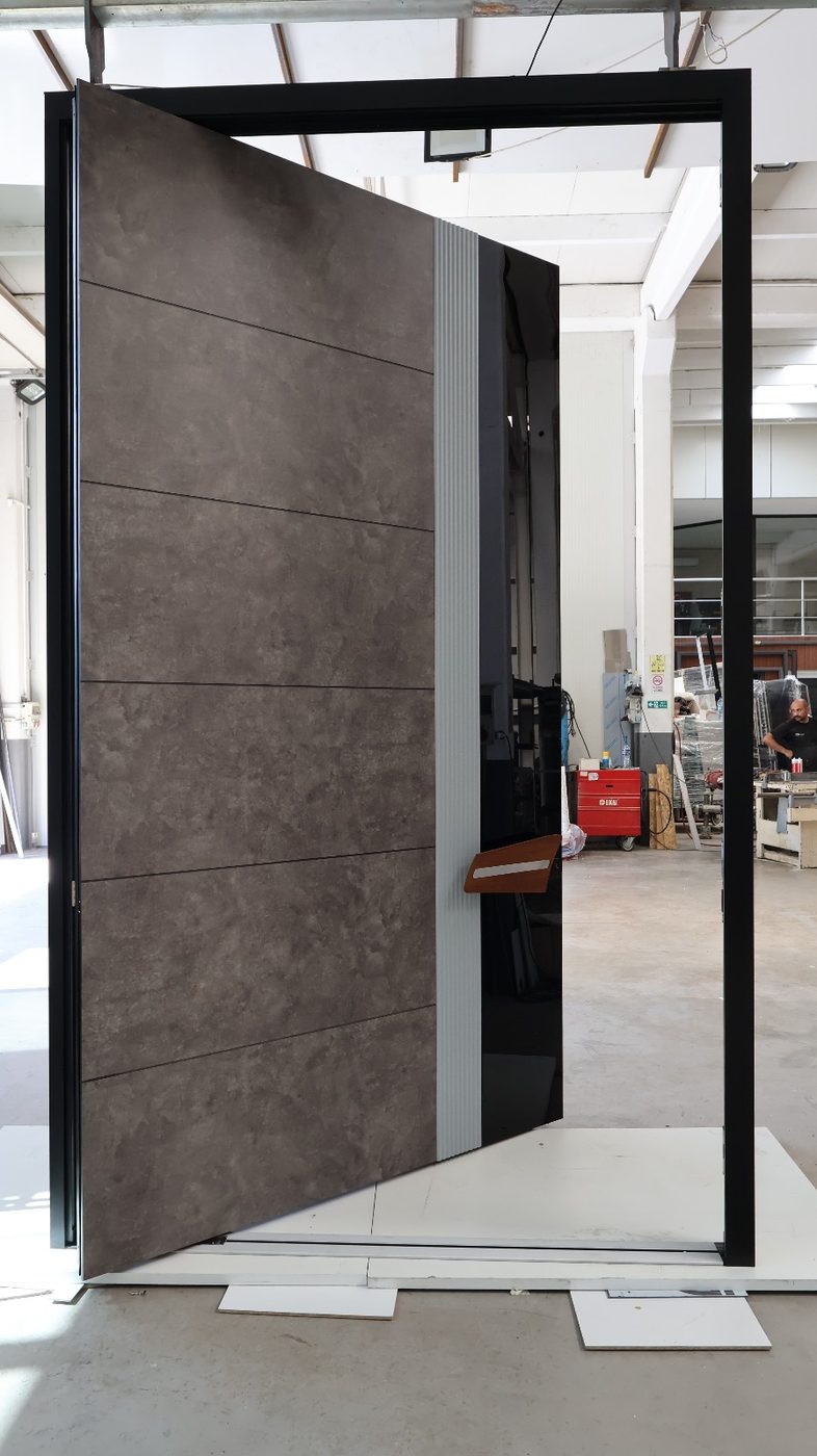 Concrete-look pivot door with a fluted aluminum strip and black glass edge, shown open
