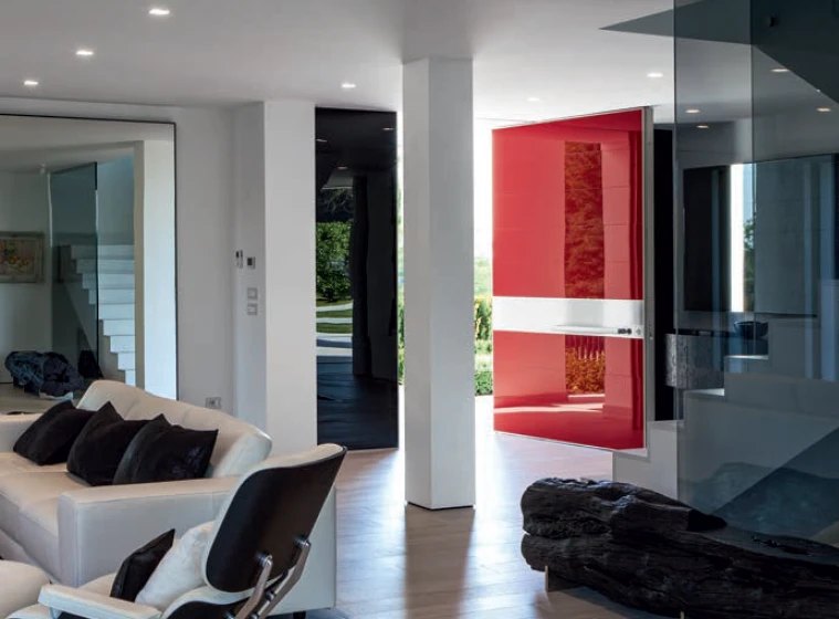Gloss red pivot door with a white band, open to the garden from a modern living room