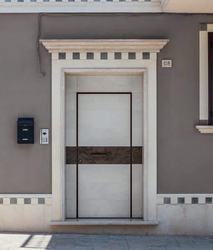 White stone-look pivot door with a bronze band set in a classical stone surround