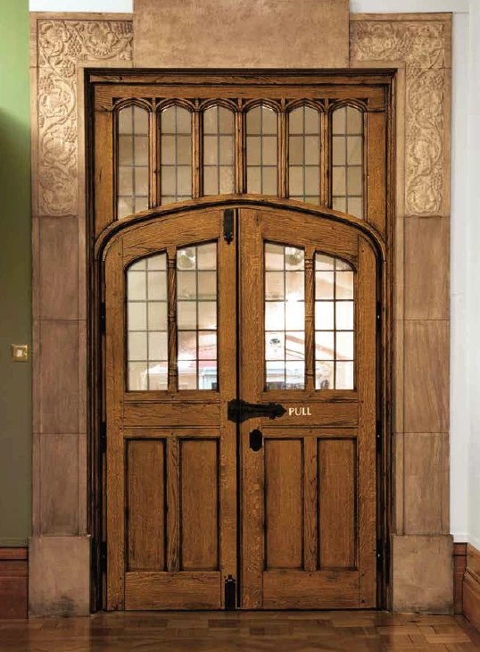 Traditional oak double door with leaded glass lites, an arched transom and hand-forged iron hardware in a carved stone surround