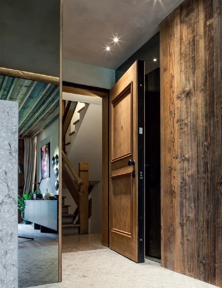 Raised-panel wood pivot door in a reclaimed-timber entry wall, shown open