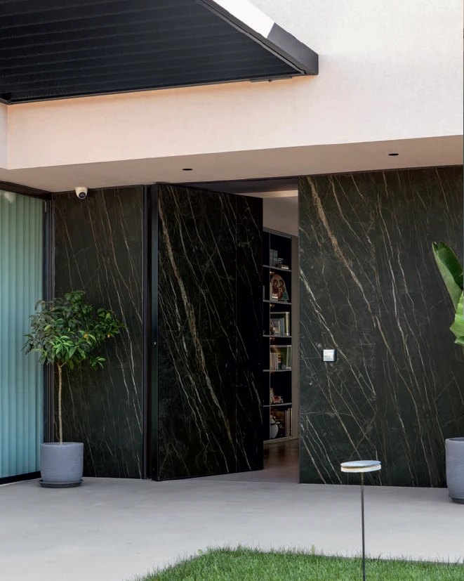 Exterior black-and-gold marble pivot door set flush in a matching marble wall, shown open